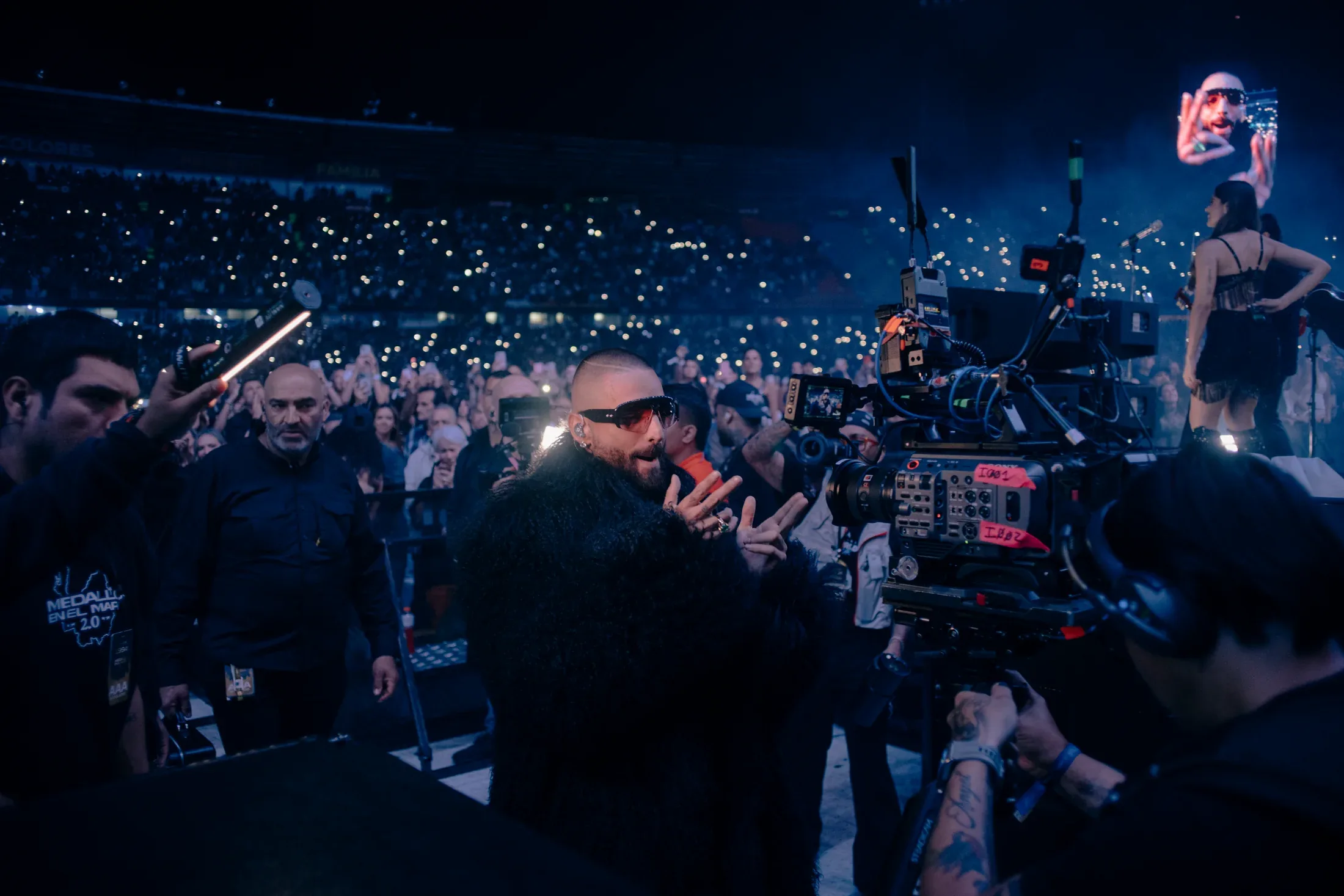 A live video director working beside a touring camera inside a concert audience.