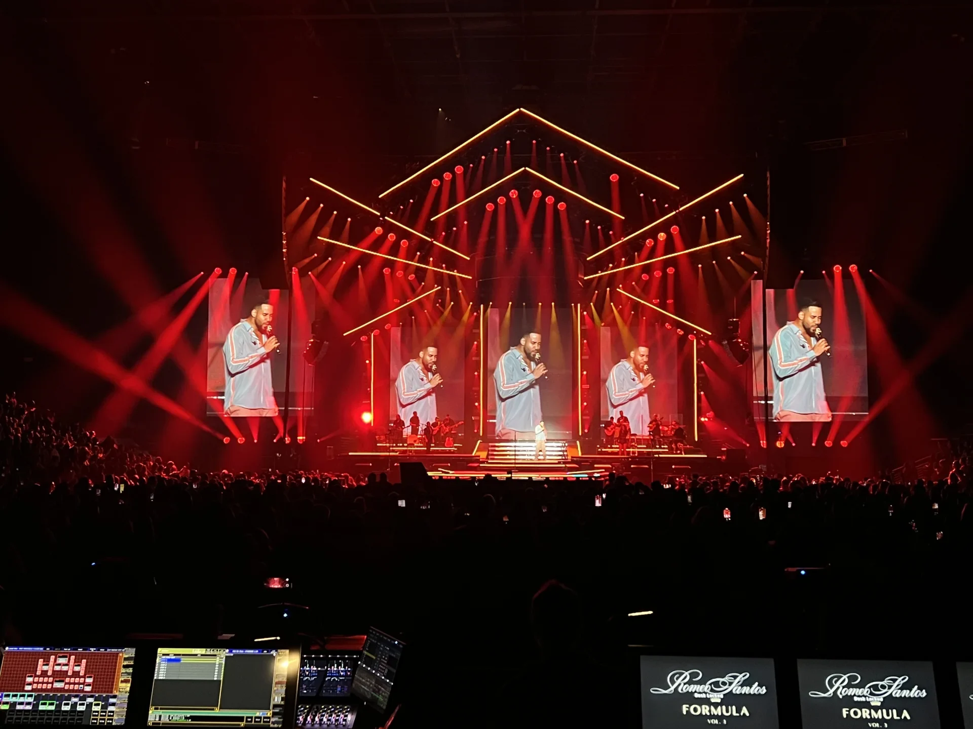 Romeo Santos performing on a red stadium stage surrounded by live screens.