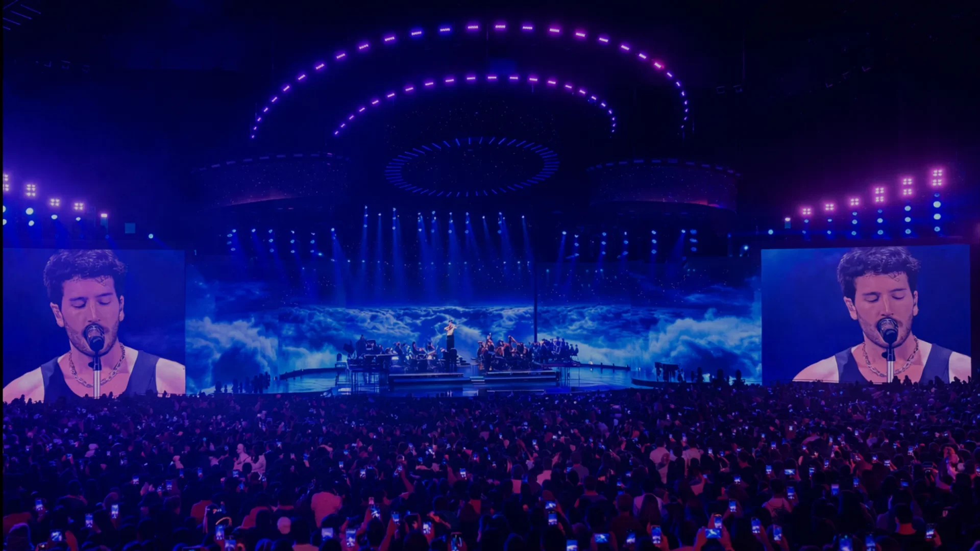 Sebastian Yatra performing on a blue arena stage surrounded by live screens.