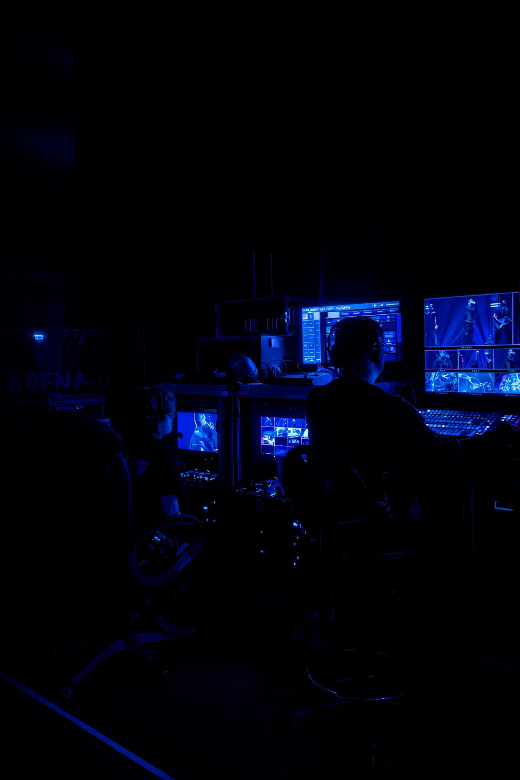 A video director working among illuminated monitors inside a dark concert control room.