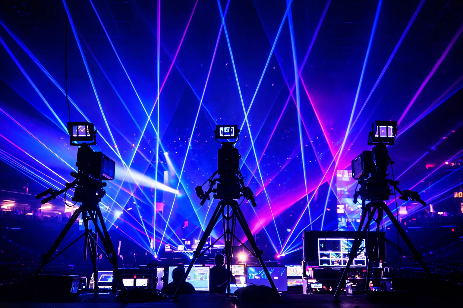 Broadcast cameras facing a concert stage crossed by blue and magenta light beams.