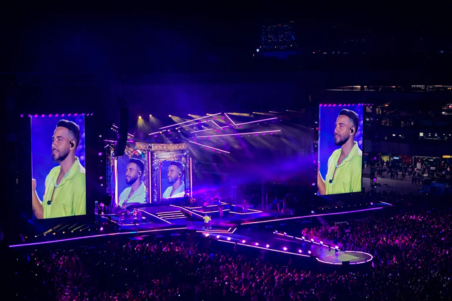 A stadium concert with large portrait screens surrounding the central stage.